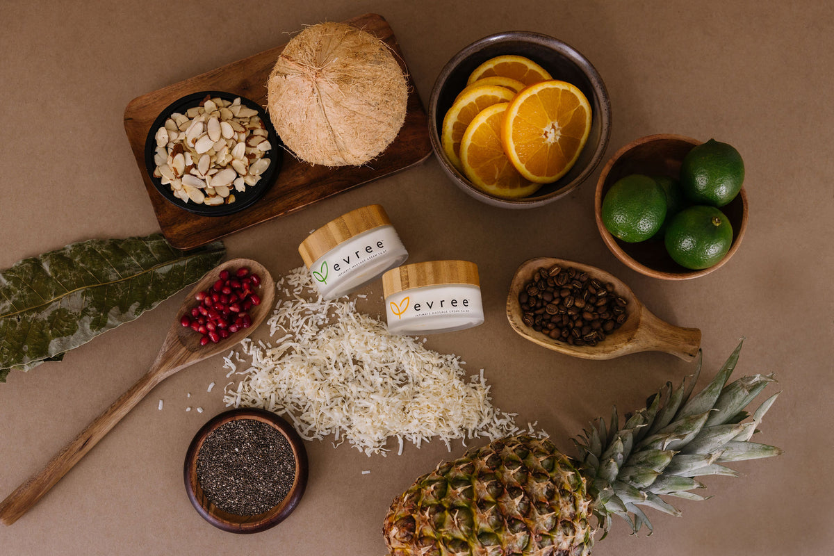Two jars of evree intimate massage cream among coconut, almonds, oranges, limes and pineapple
