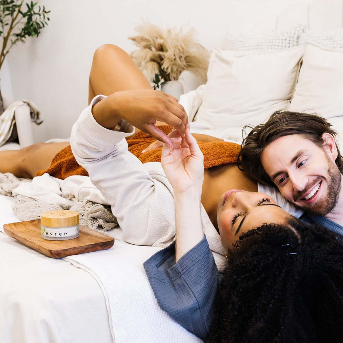 Smiling couple lying together on a bed with a jar of evree on a wooden tray beside them