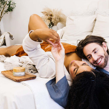 Smiling couple lying together on a bed with a jar of evree on a wooden tray beside them