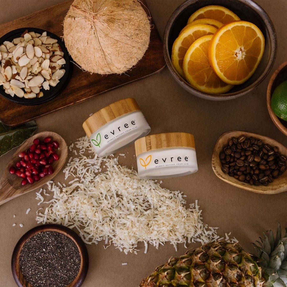 Two jars of evree intimate massage cream among coconut, almonds, oranges, pomegranate seeds and pineapple
